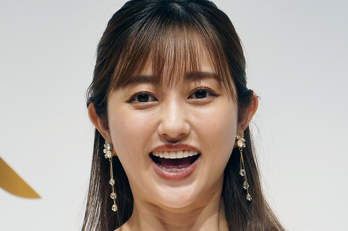 白いオフショルダードレスを着た女性が笑顔でカメラに向かっている。
