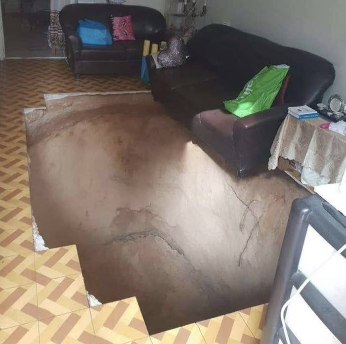 Living room with a large, deep sinkhole in the floor, surrounded by sofas and a table