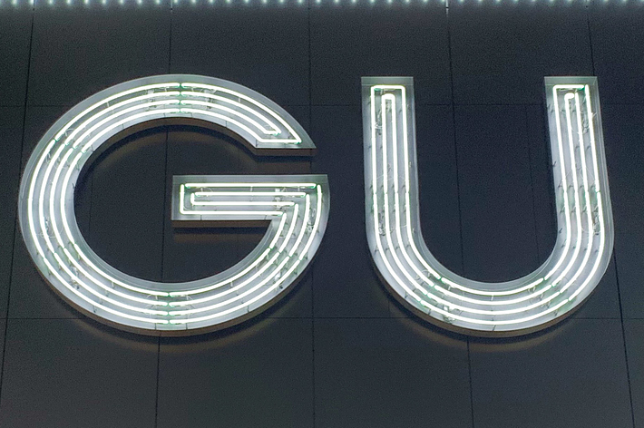 GU sign illuminated with neon lights against a dark background