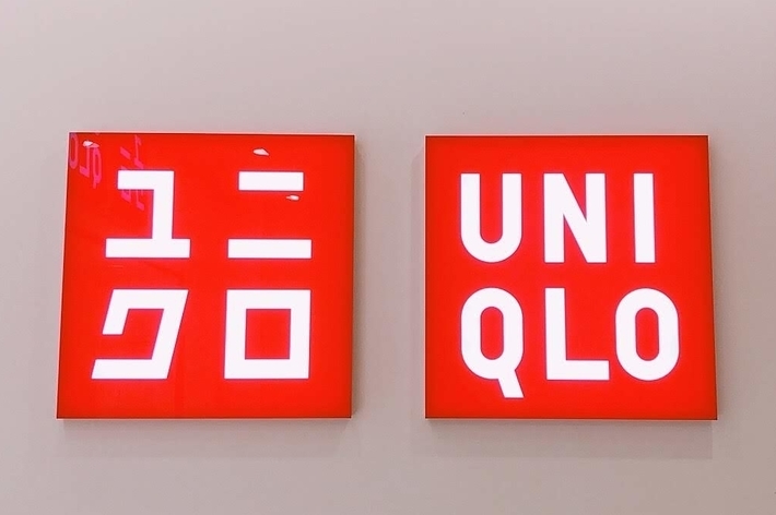 Two red signs on a wall. The left sign has Japanese characters, and the right sign reads &ldquo;Uniqlo&rdquo; in bold white letters