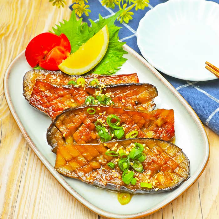 皿に盛られたナス、トマトのスライス、レモン、青葉が添えられている。