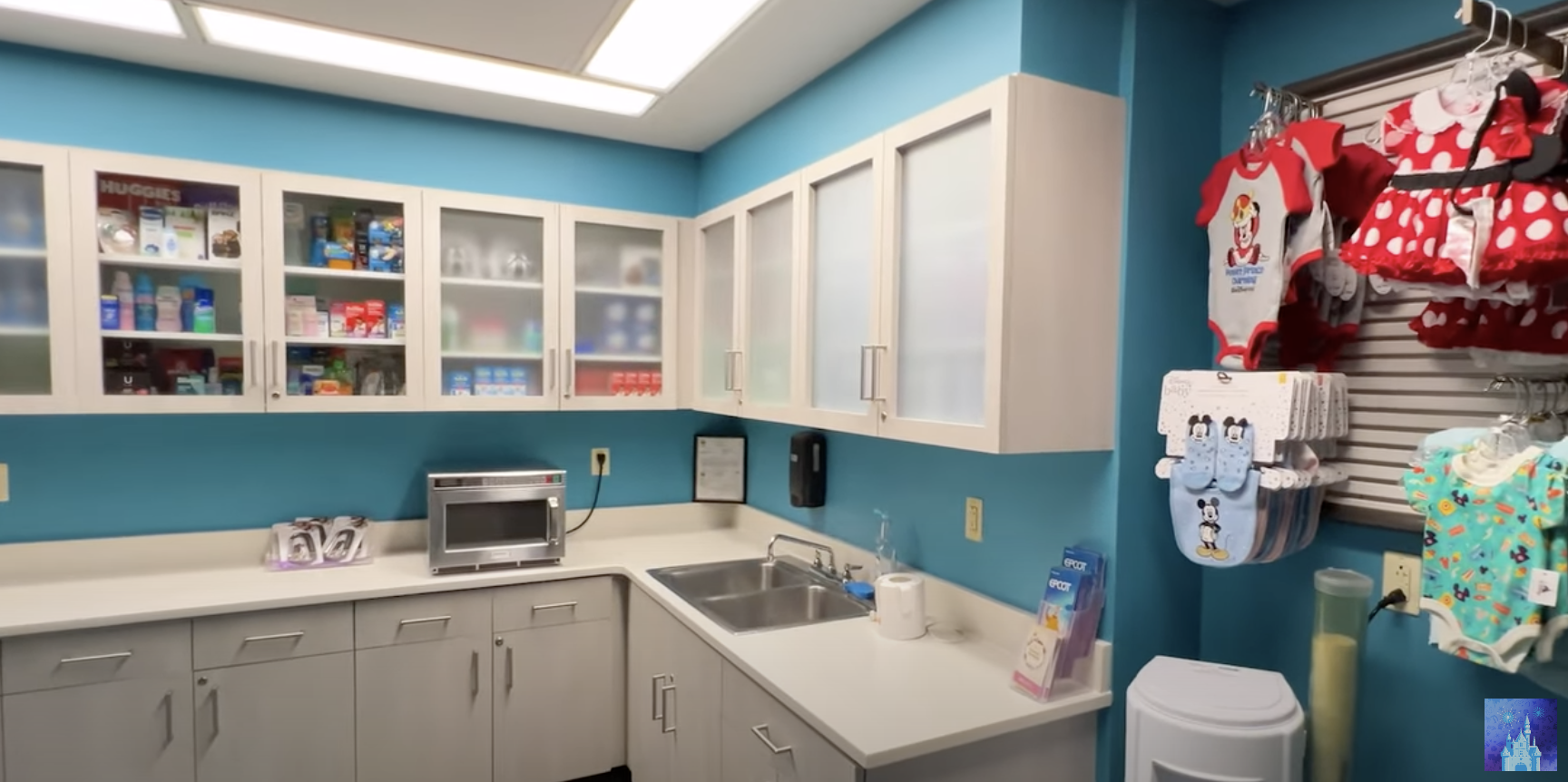 A tidy, well-organized clinic room, with medical supplies in glass cabinets, a microwave, sink, and Disney-themed children's clothes hanging on the wall