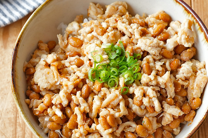 鶏そぼろと納豆の丼が木製テーブルの上に置かれている。刻んだネギが中央に載っている。