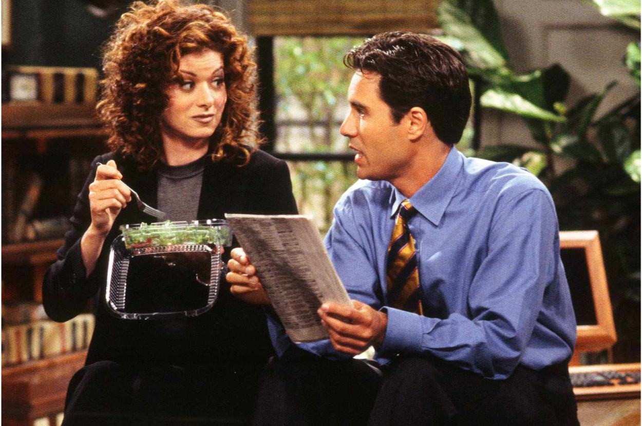Debra Messing, holding a salad container, and Eric McCormack, reading a newspaper, in a scene from a TV show