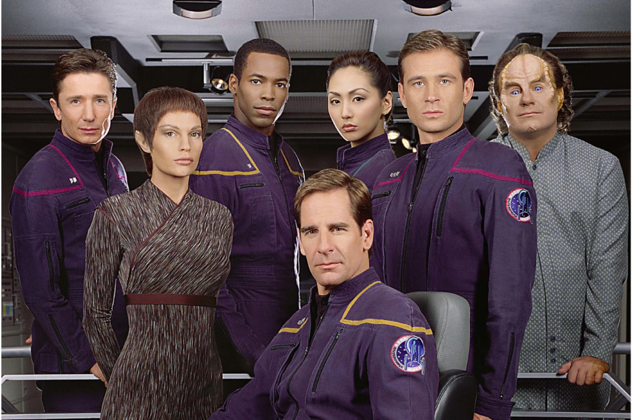 Scott Bakula, Jolene Blalock, Dominic Keating, Anthony Montgomery, Linda Park, Connor Trinneer, and John Billingsley in sci-fi uniforms on a spaceship set