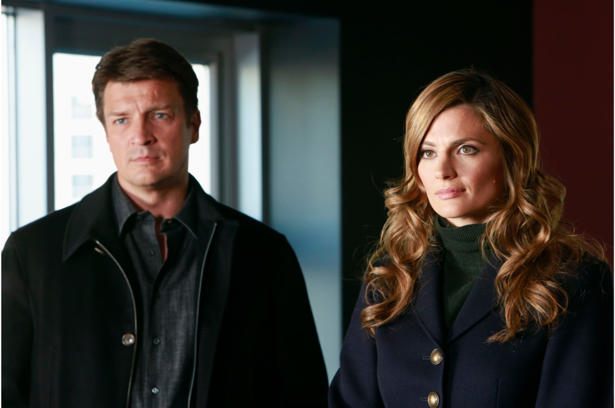 Nathan Fillion and Stana Katic in a serious scene, standing indoors with a focused look, wearing formal attire