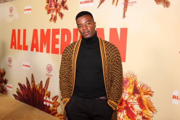 Daniel Ezra poses on the red carpet at the "All American" event, wearing a patterned cardigan over a turtleneck shirt