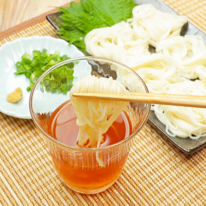 ガラスの器に入ったそうめんを箸で持ち上げ、左側に細かく刻んだネギが添えられた小皿がある。