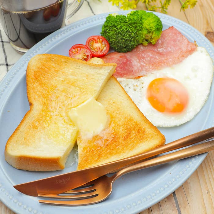 トースト、バター付き、目玉焼き、ブロッコリー、ミニトマト、コーヒーの朝食セット。