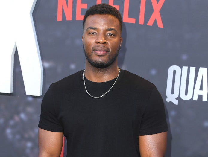 Closeup of Daniel Ezra on the red carpet wearing a plain T-shirt and a thin chain