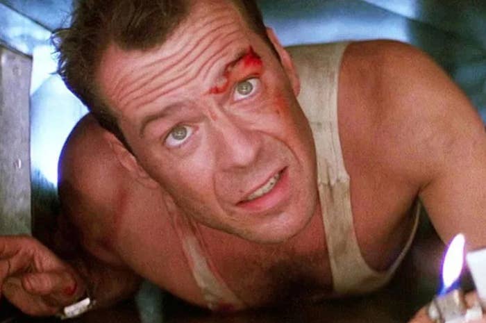 Bruce Willis crawling through metal duct, holding a lighter, with a cut on his forehead, in a scene from "Die Hard"