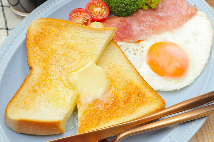 トースト、バター、目玉焼き、ベーコン、ブロッコリー、ミニトマトが盛り付けられた朝食プレートとコーヒーのセット。