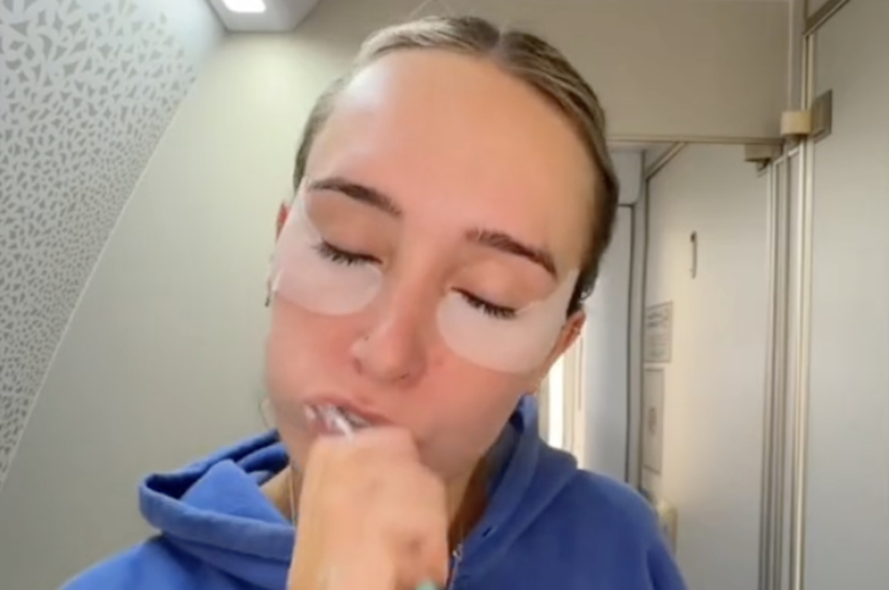 女性が飛行機の洗面台で歯を磨いている様子。上部に「i told the woman in the queue i would be 2 minutes...」とテキスト。時間は7:58:15と記載。