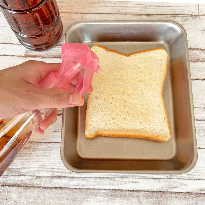 手にスプレーボトルを持ち、食パンにスプレーしている様子。