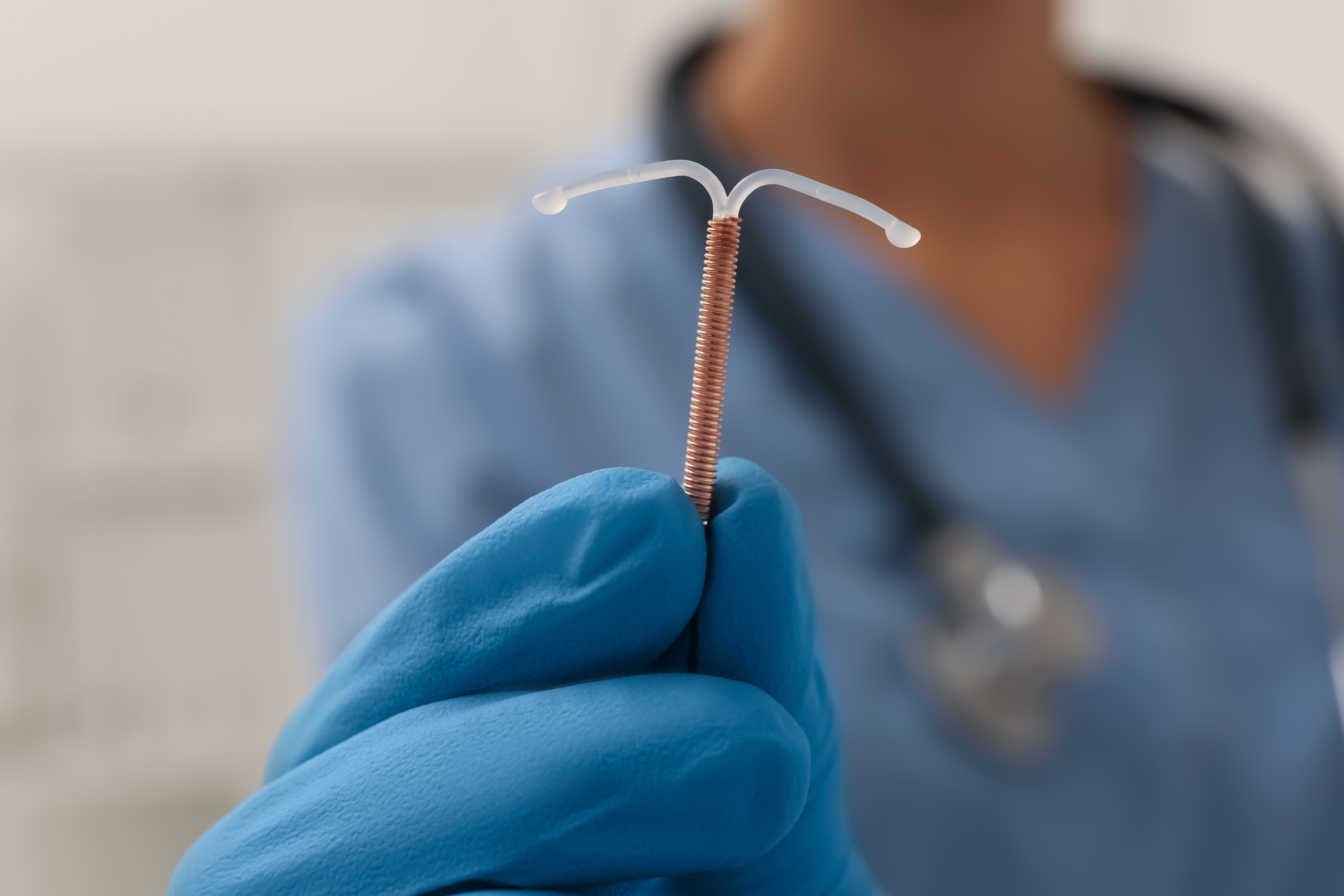 A person in scrubs and gloves holds an intrauterine device (IUD) close to the camera