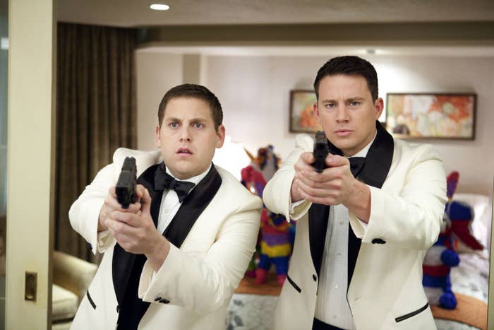 Jonah Hill and Channing Tatum in tuxedos, aiming guns, with piñatas in the background in a scene from 21 Jump Street