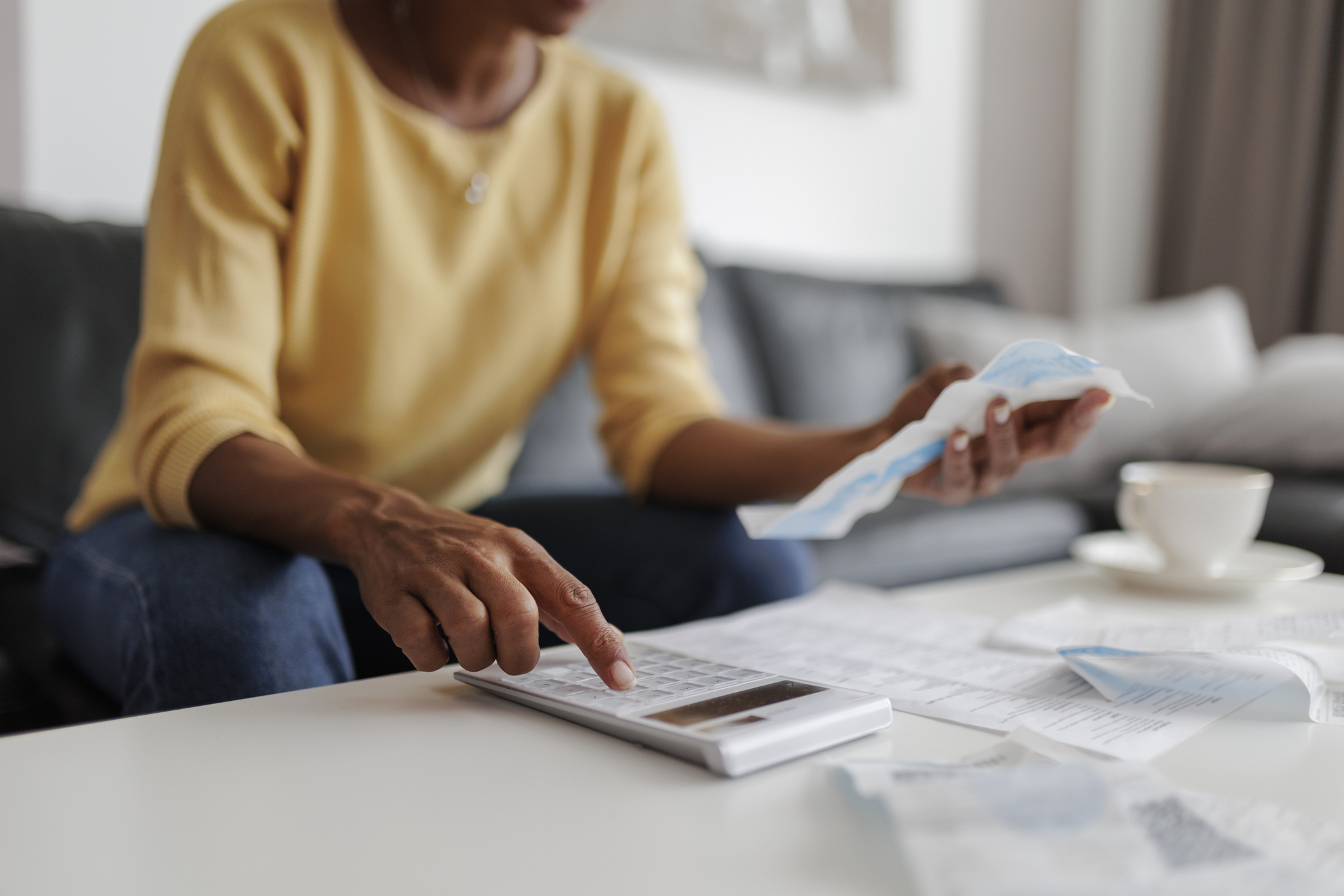A person sits at a table using a calculator, surrounded by receipts and documents, likely managing finances