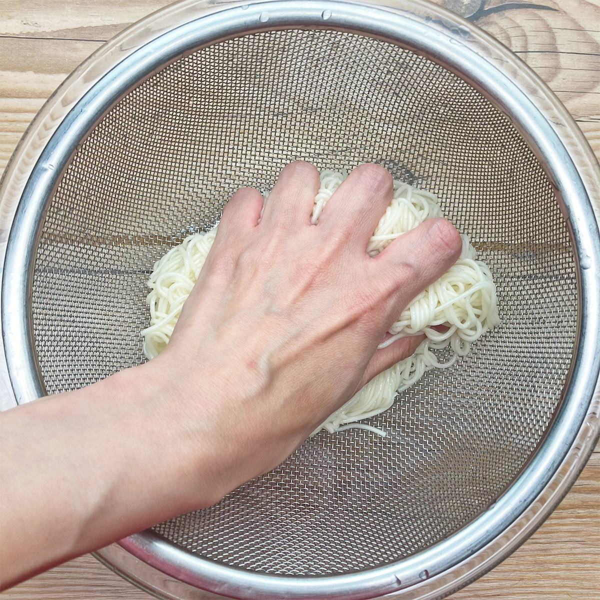 手がざるの中で麺をすすいでいる様子。