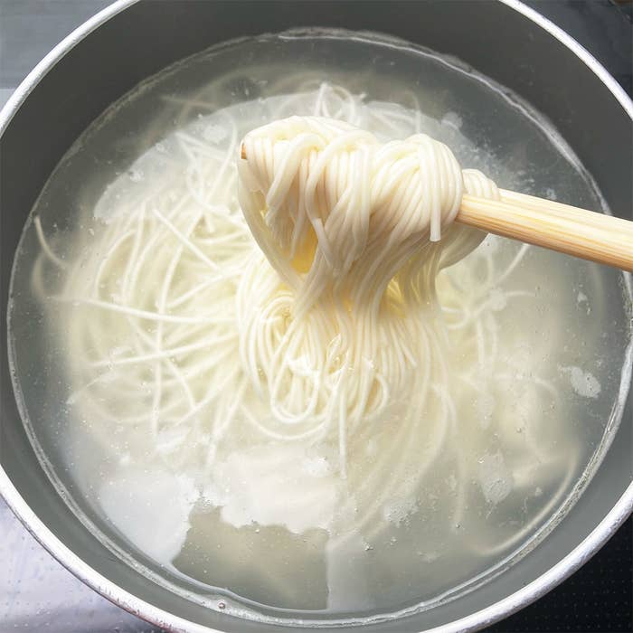 鍋の中で茹でられているそうめんが箸で持ち上げられている。