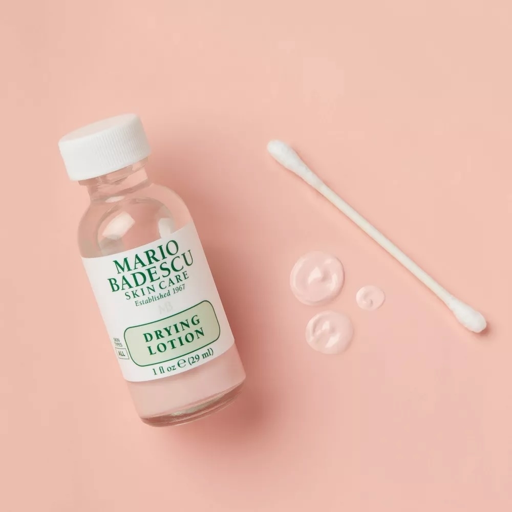 Mario Badescu Drying Lotion bottle with a cotton swab and three drops of lotion on a plain background