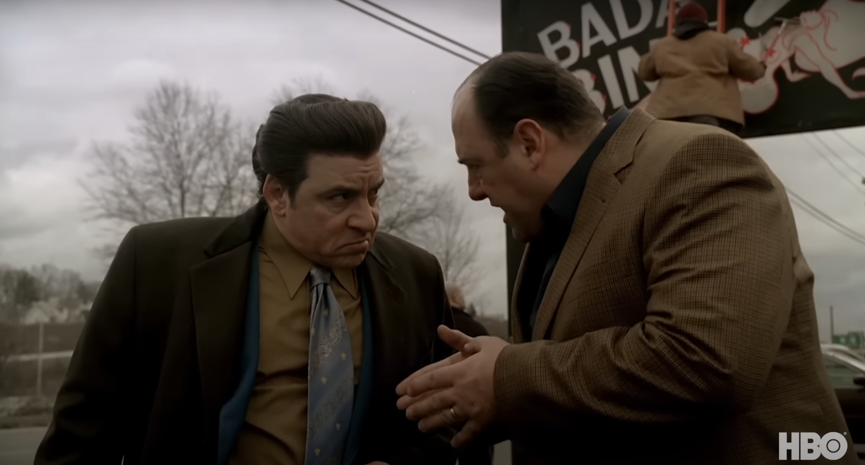 Steven Van Zandt and James Gandolfini in a scene from HBO's "The Sopranos," engaged in a serious conversation outdoors near a sign that reads "Bada Bing."