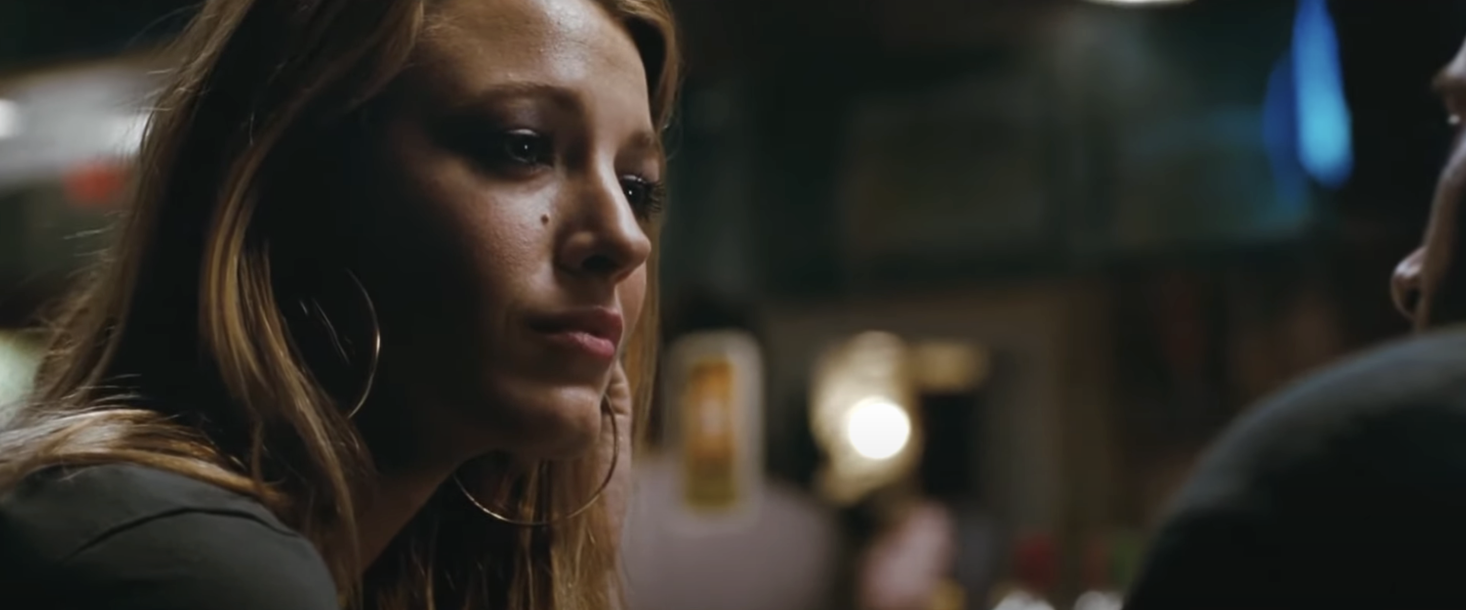Blake Lively in a contemplative scene, wearing hoop earrings. She gazes off to the side with a thoughtful expression