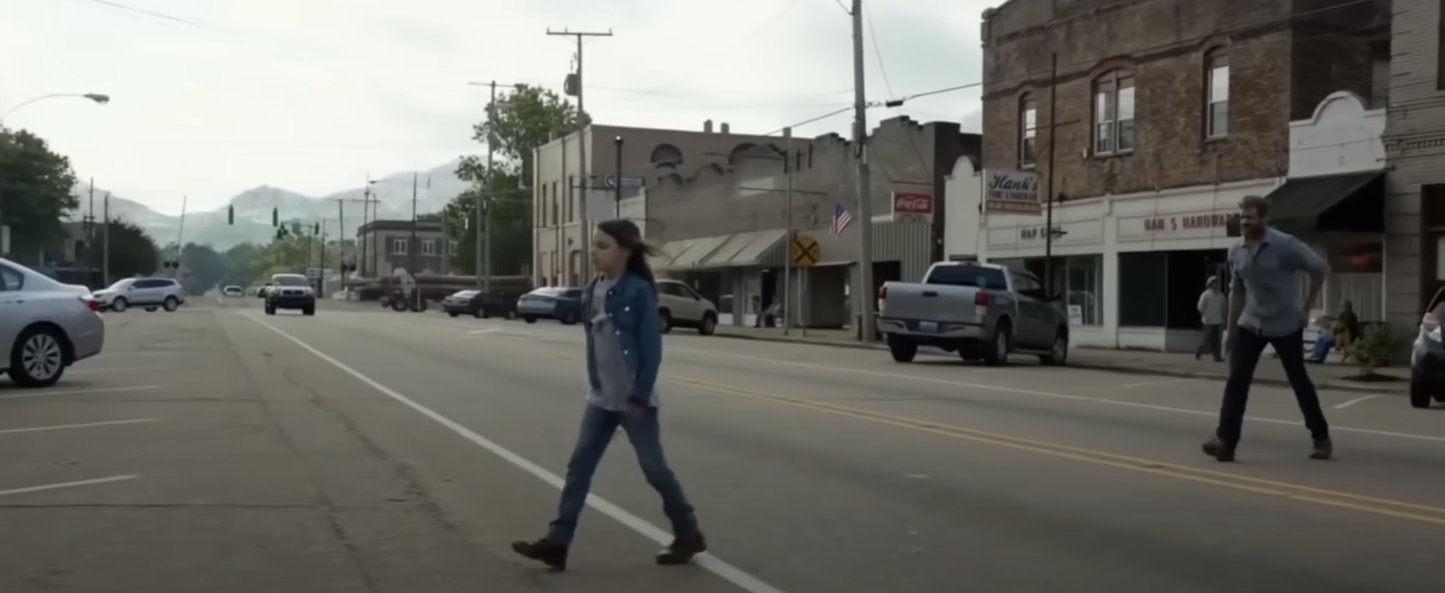 Logan follows Laura across the downtown street, mountains and trees in background