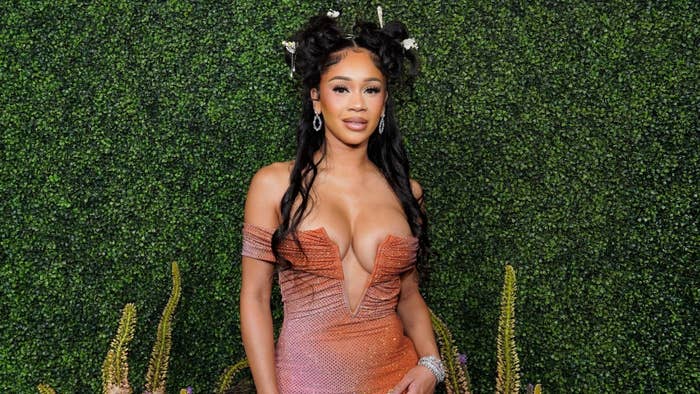 Saweetie stands in front of a leafy backdrop, wearing a strapless, plunging dress with floral accessories in her hair