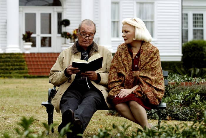 James Garner reads a book while sitting on a bench with Gena Rowlands, who is wearing a shawl. They are in front of a house in a scene from The Notebook