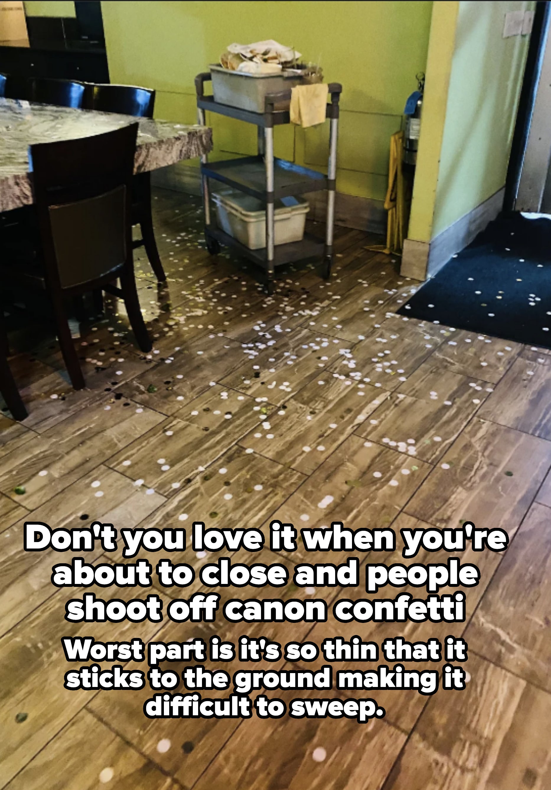 A restaurant floor scattered with confetti, in front of a table and a utility cart with cleaning supplies