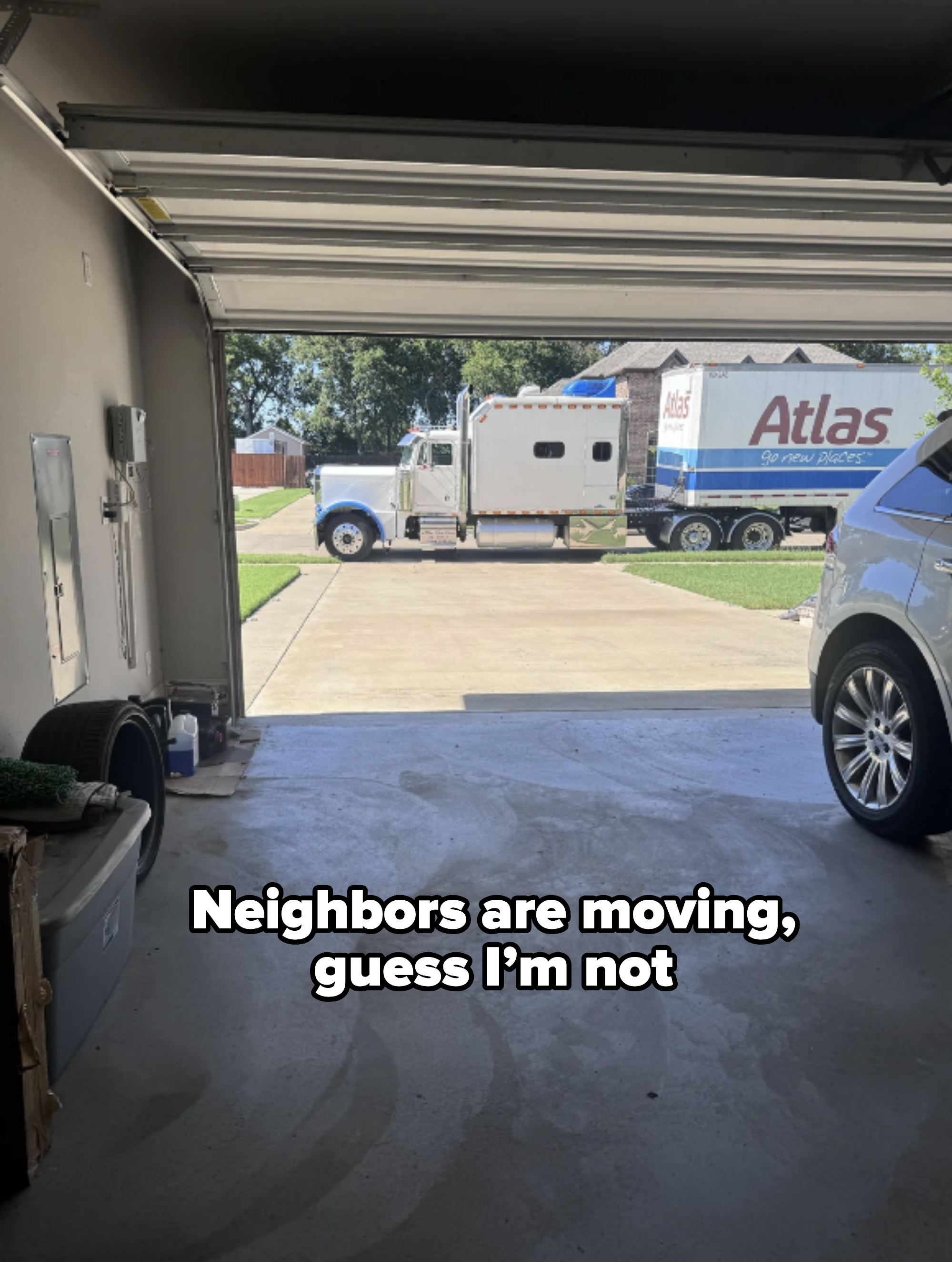 View from inside a garage looking out to a driveway where a moving truck labeled &quot;Atlas&quot; is parked