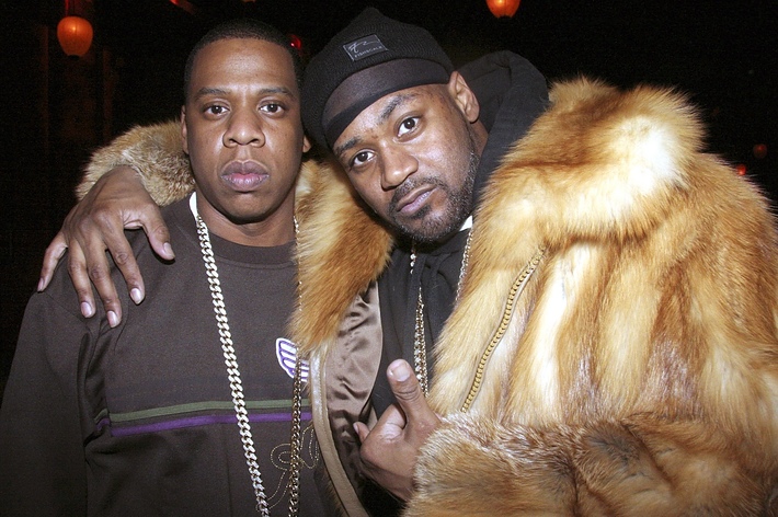 Jay-Z in a dark sweater and chain necklace, and Ghostface Killah in a fur coat and beanie, posing together with Jay-Z's arm around Ghostface Killah's shoulder