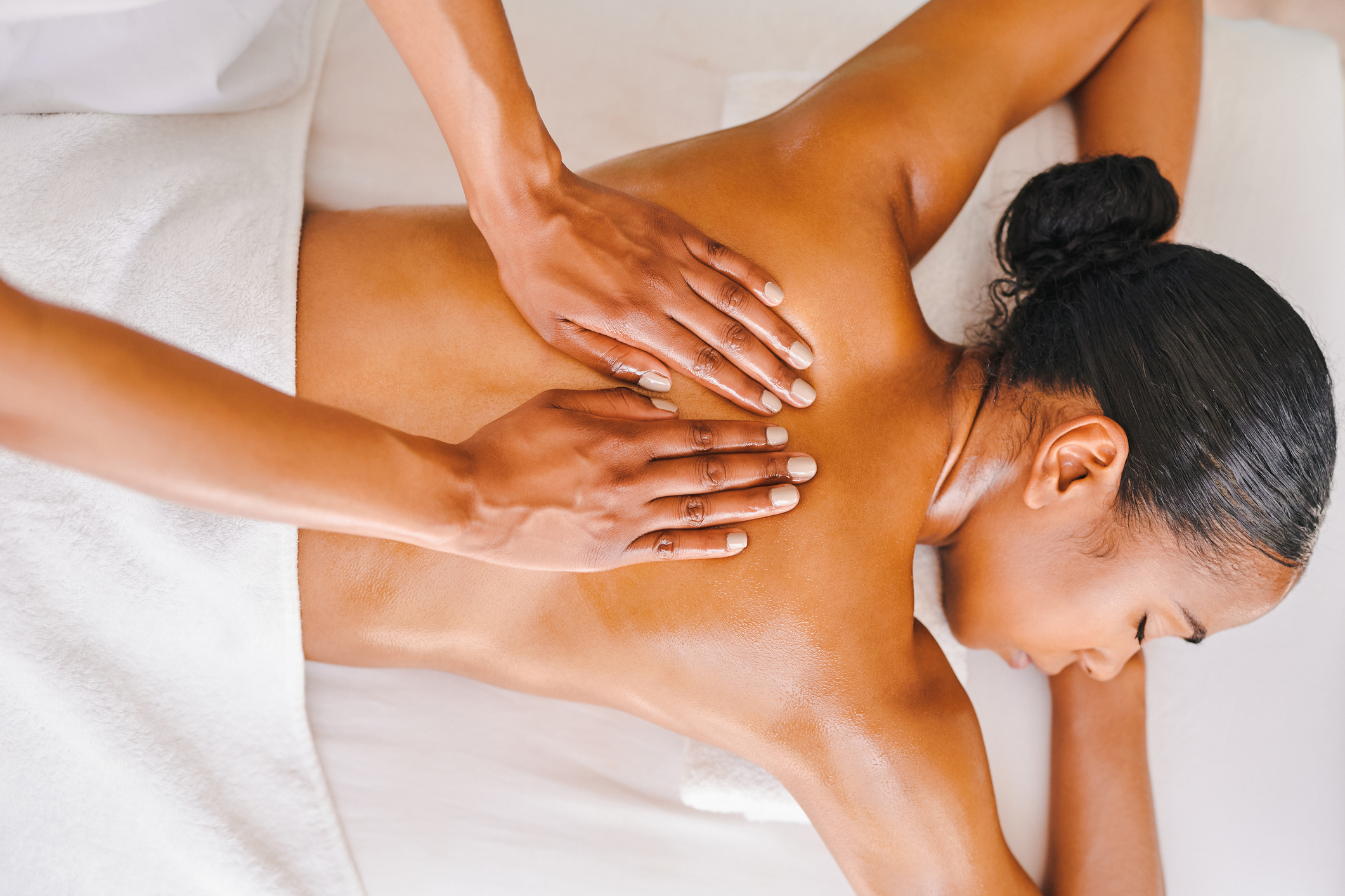 Person receiving a back massage while lying face down on a table covered with a white towel. Hands are shown massaging the person's back
