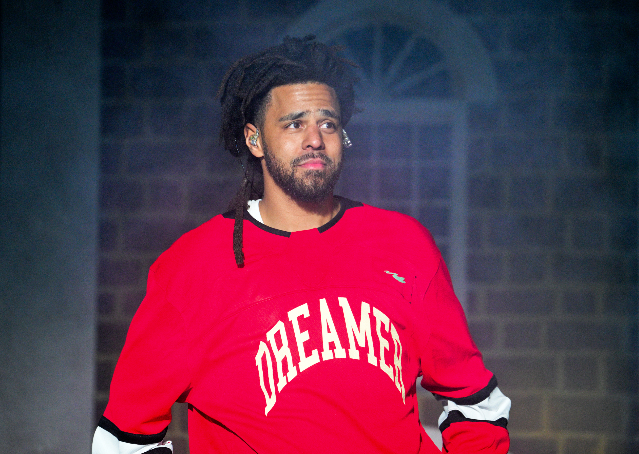 J. Cole on stage wearing a &quot;Dreamer&quot; jersey, performing during a concert