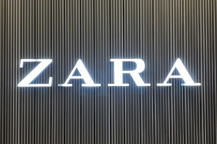 &ldquo;ZARA store sign with illuminated letters on a vertical striped background.&quot;