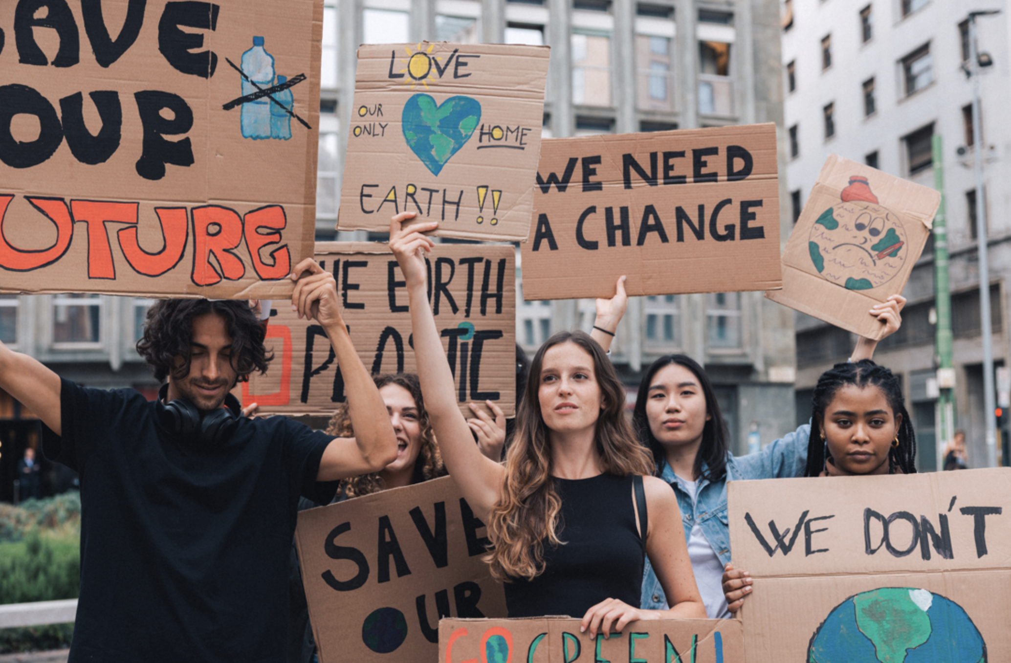 People holding signs advocating for environmental change with phrases like &quot;Save our future,&quot; &quot;Love our Earth,&quot; &quot;We need a change,&quot; and &quot;We don't have time&quot;