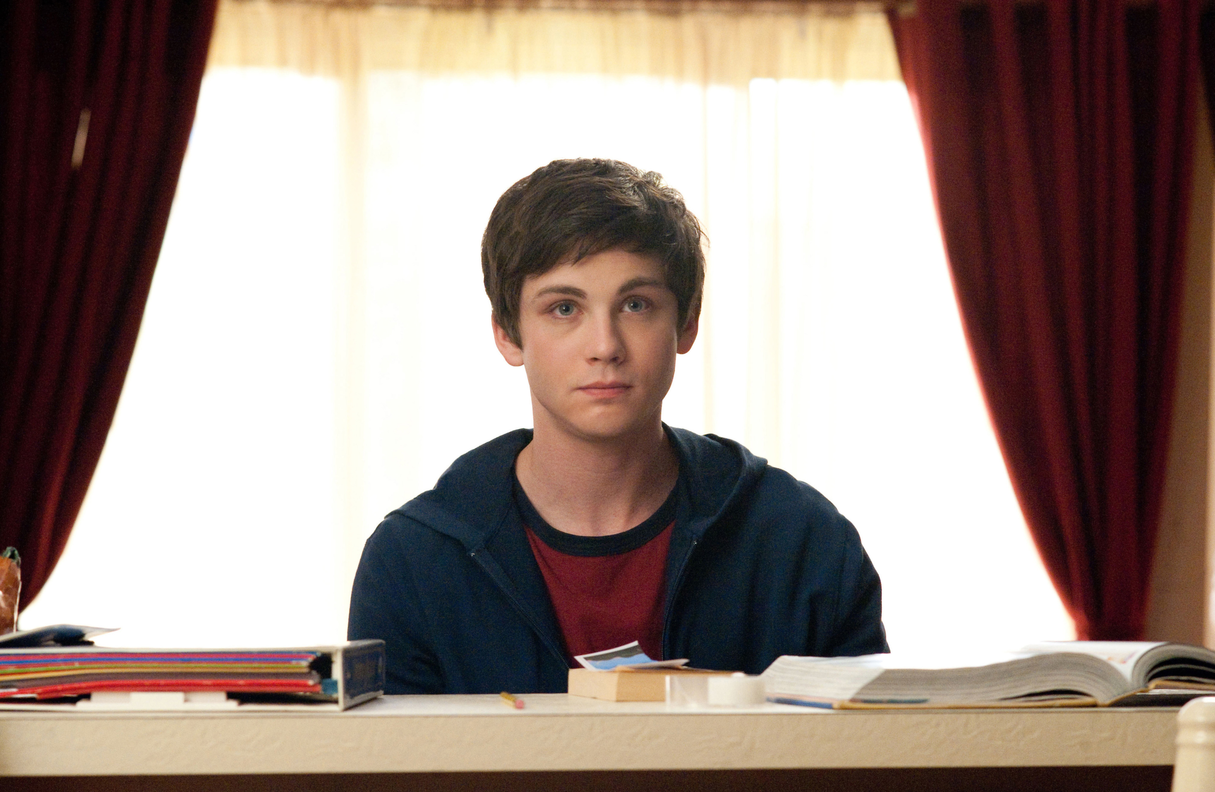Logan Lerman sits at a desk with books and papers in front of him, looking thoughtful in a scene from &quot;The Perks of Being a Wallflower&quot;