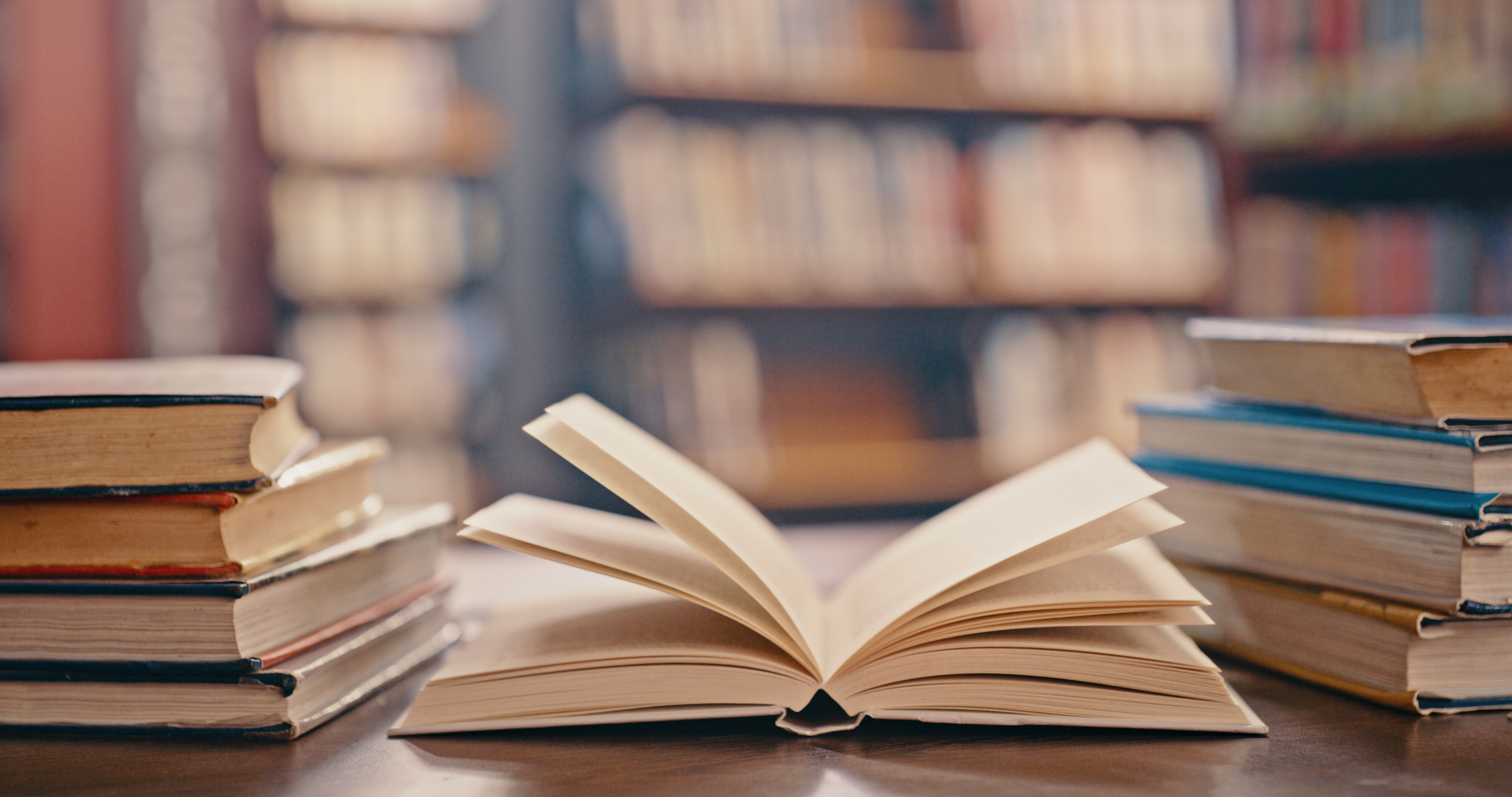 Open book on a table with stacks of books on either side in a library setting
