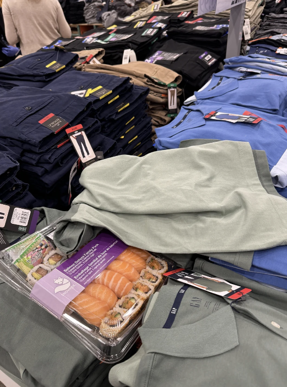 Casual men's clothing like pants and shirts displayed on a store table, with a package of sushi placed on top of the clothes