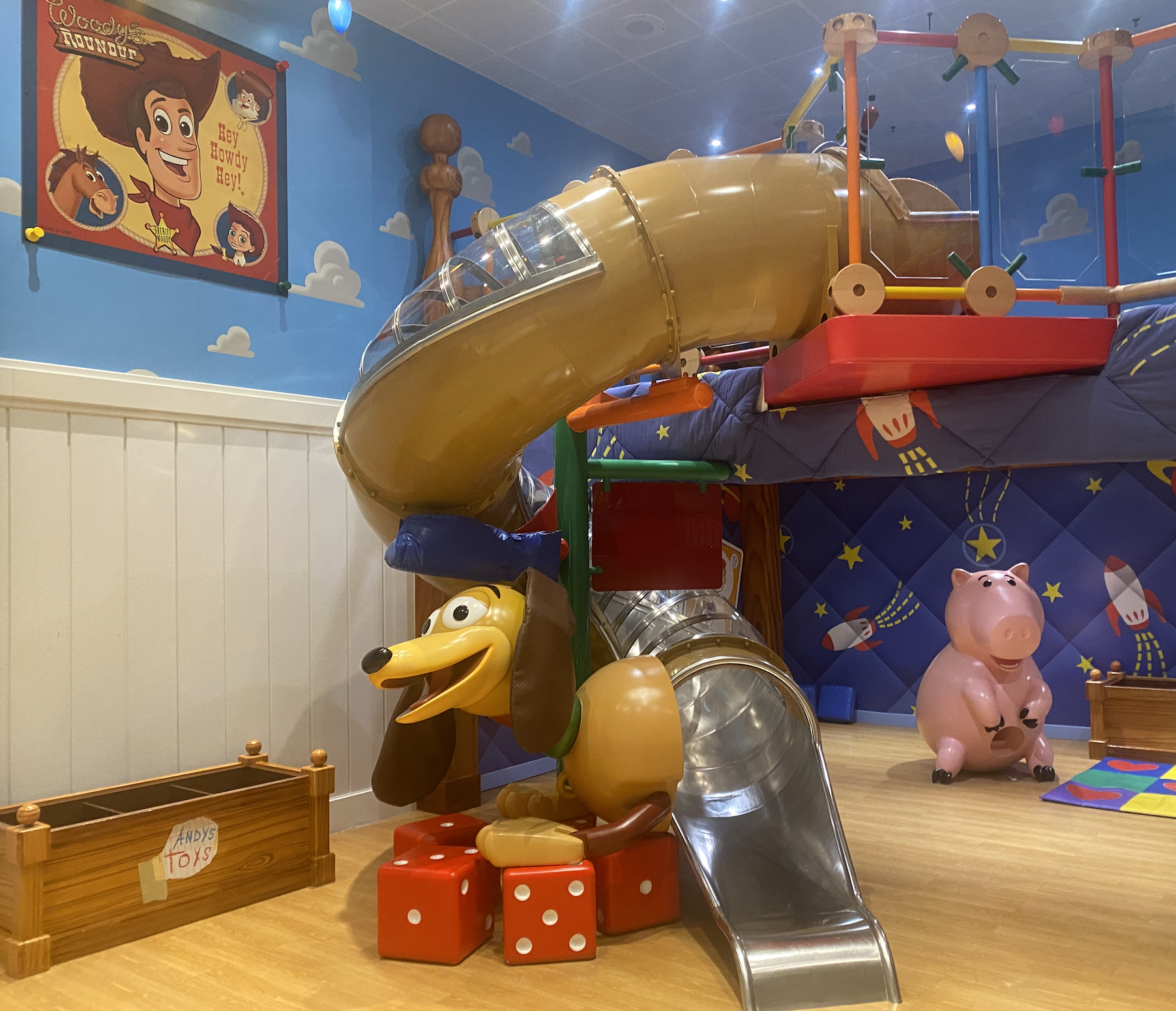 Children&#x27;s play area with Toy Story-themed decor, including Woody poster, tunnel slide, Slinky Dog slide, and Hamm piggy bank figure