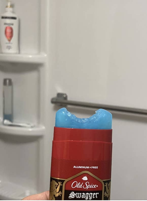 A stick of Old Spice Swagger deodorant with a bite mark. Shower products are visible on a bath shelf in the background