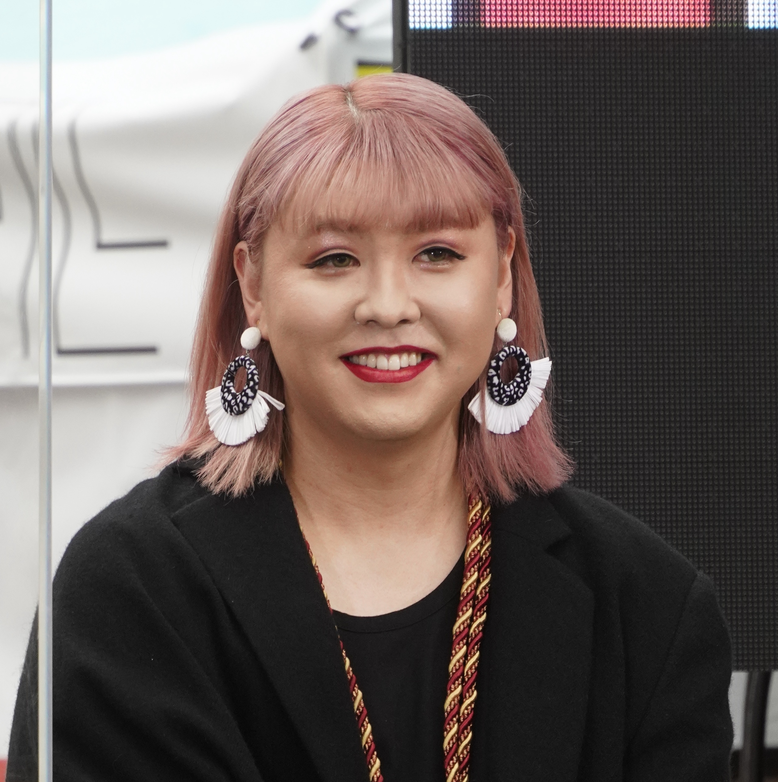 女性が笑顔でカメラを見ています。名前はわかりません。大きなイヤリングを身につけ、黒い服を着ています。