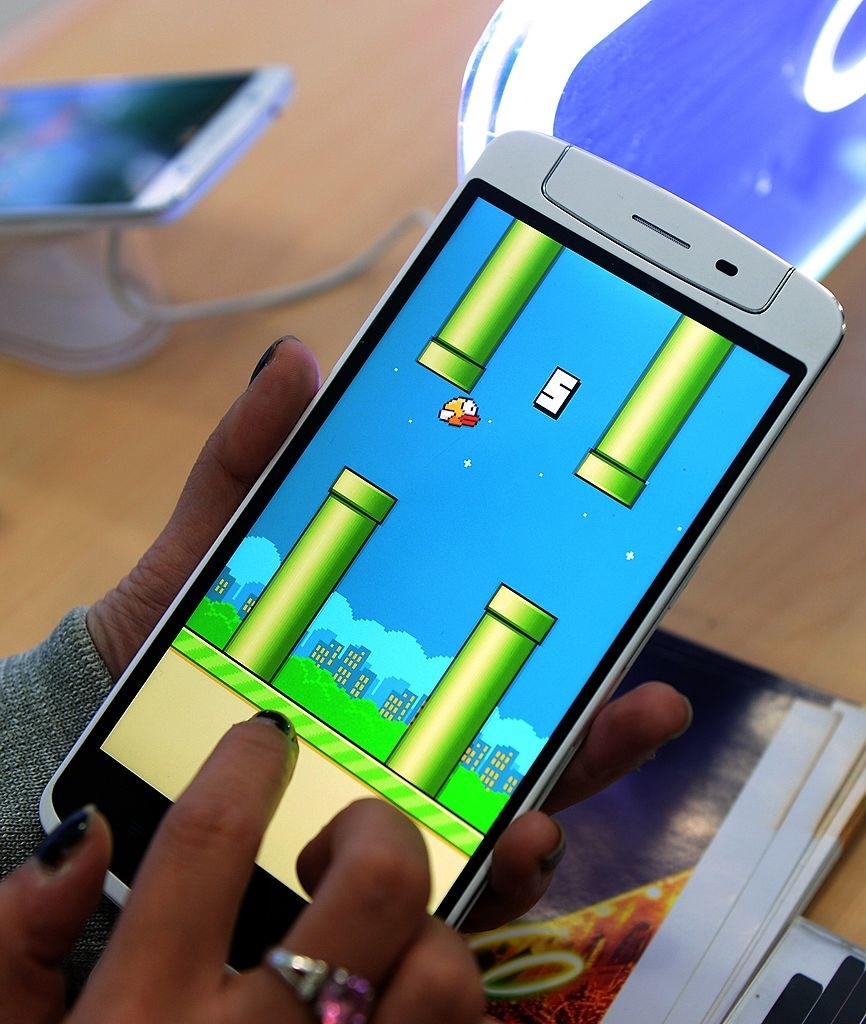 Close-up of hands playing the game Flappy Bird on a smartphone touchscreen