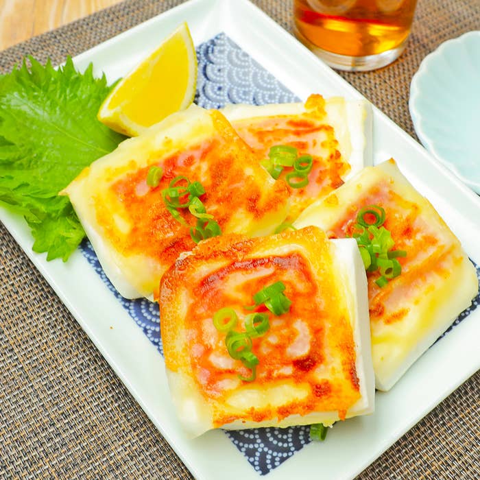 皿に盛られた焼かれた料理、上に刻んだネギとレモンのくし切りが添えられている。