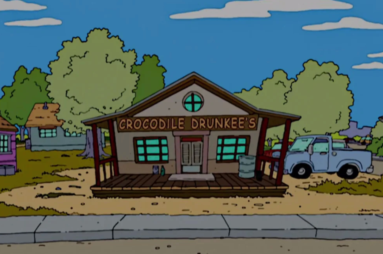Front view of Crocodile Dunkee's bar with a watering can and barrel on the porch, a pickup truck parked beside it, and surrounding trees