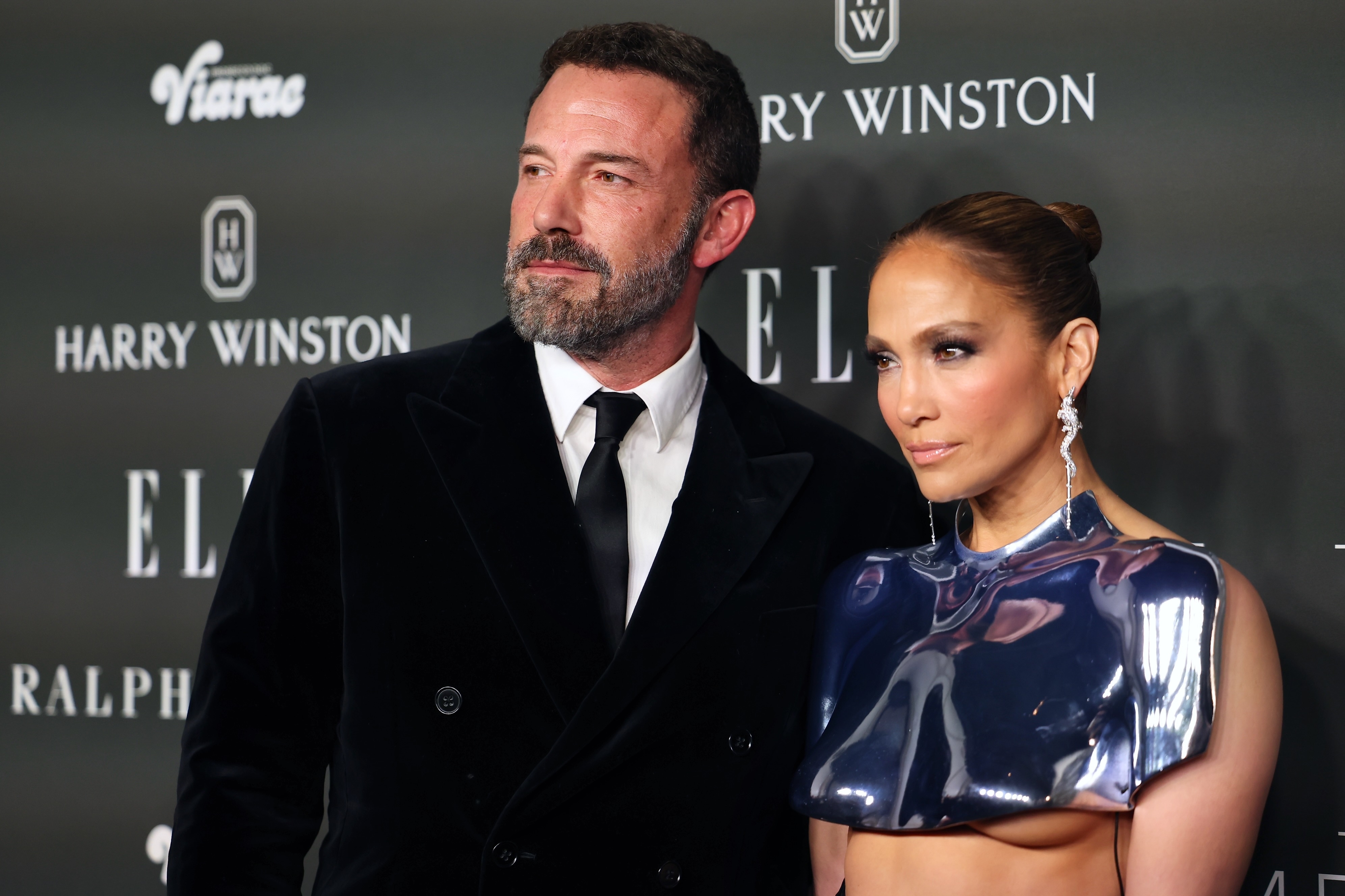 Ben Affleck and Jennifer Lopez on the red carpet. Ben is wearing a black suit and tie; Jennifer is wearing a futuristic metallic top