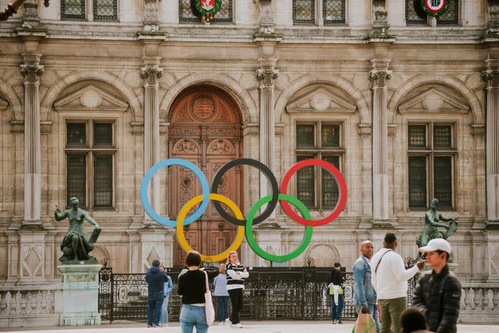 People are seen successful  beforehand   of a gathering  with ample  Olympic rings displayed connected  it. The representation  depicts a sports-related scene. Names of circumstantial  individuals are not provided