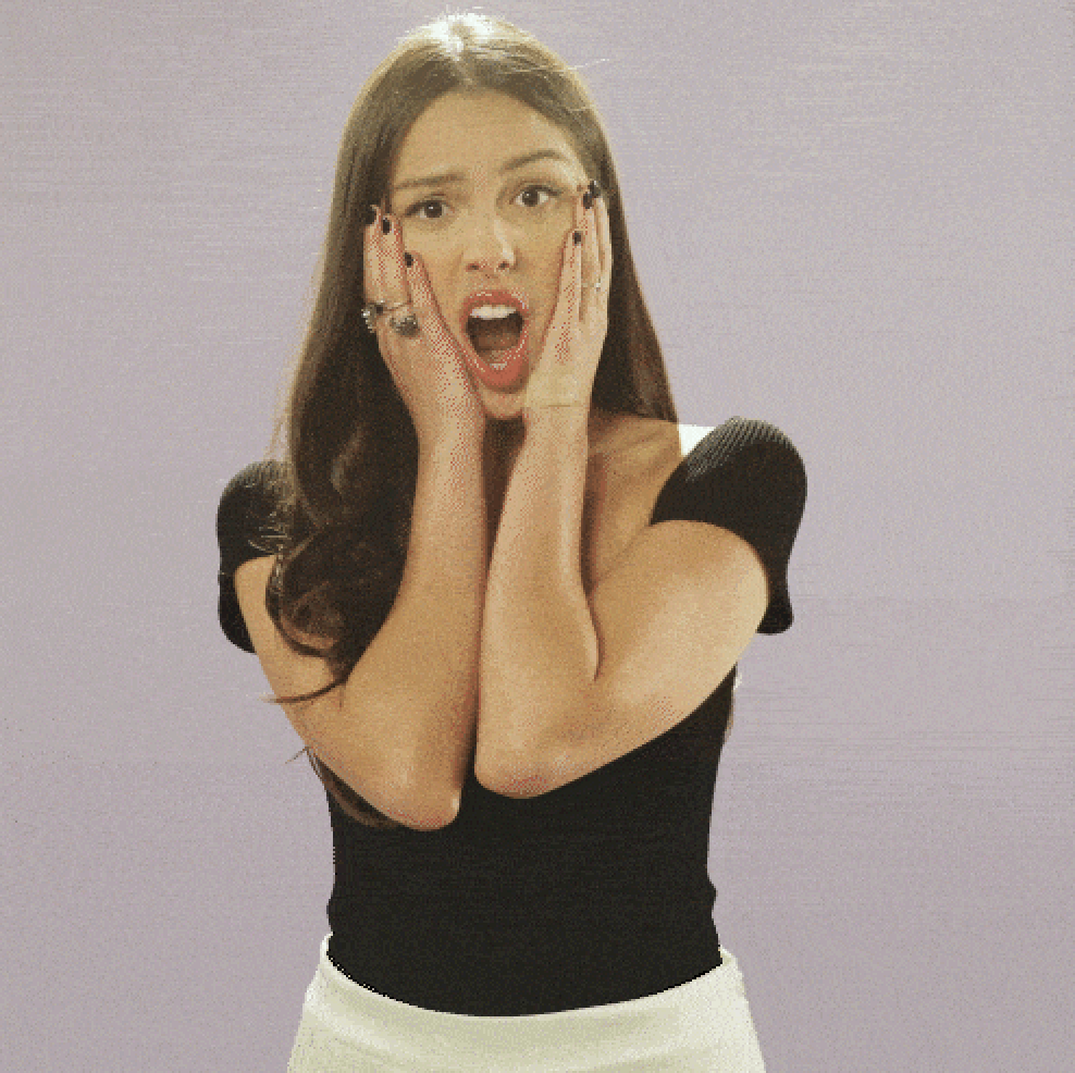 Woman with long hair, wearing a black top and white skirt, holds her face with both hands, expressing shock or surprise