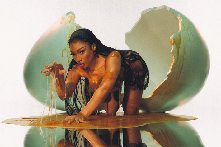 Megan Thee Stallion poses on all fours in front of a giant cracked egg, covered in a liquid resembling yolk