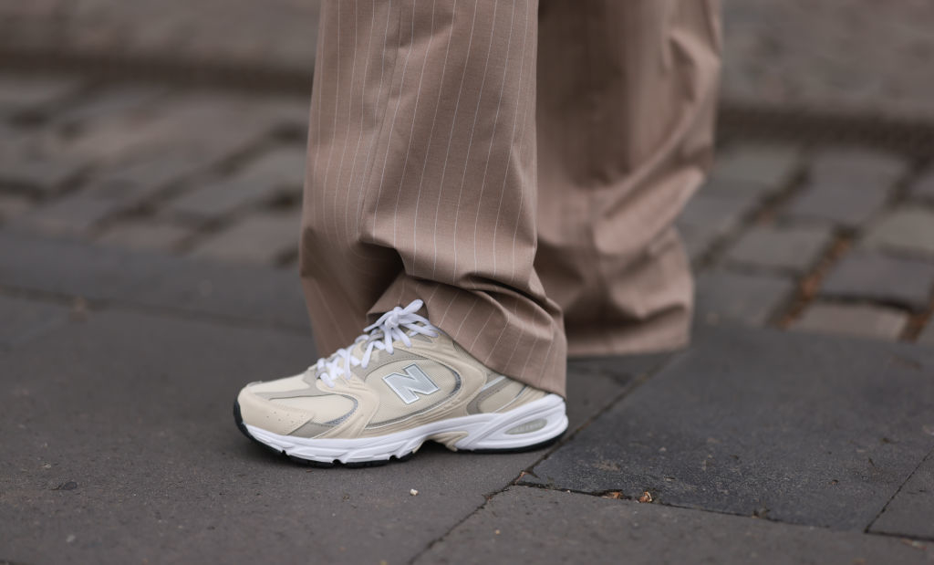 Close-up of a person's foot wearing beige sneakers with the letter N on the side, paired with beige pinstripe pants